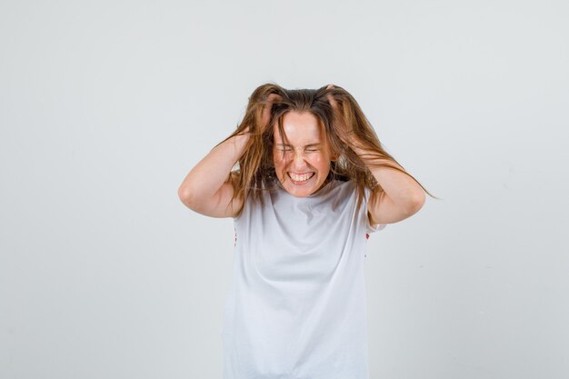 Hembra joven sosteniendo mechones de su cabello en camiseta blanca