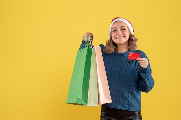 Hembra joven sosteniendo una tarjeta bancaria y paquetes después de comprar en amarillo