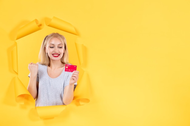 Hembra joven con tarjeta de crédito en la superficie de papel amarillo rasgado