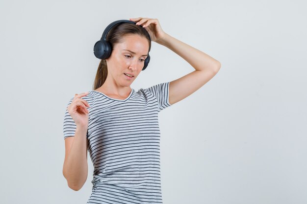 Hembra joven tocando auriculares en camiseta a rayas y mirando pensativo. vista frontal.