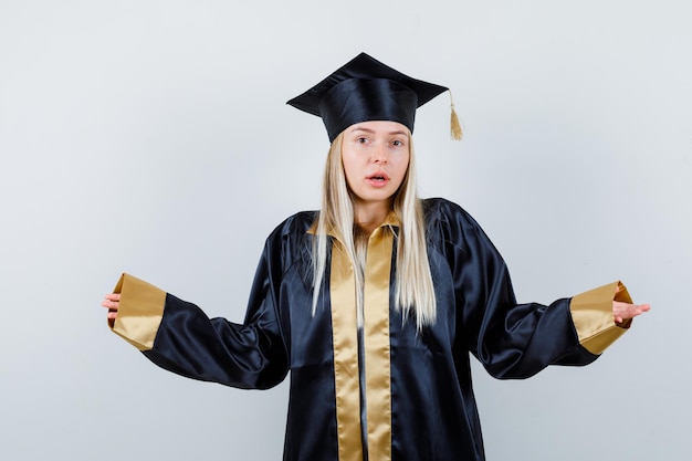 Foto gratuita hembra joven en uniforme de posgrado que muestra un gesto de impotencia y parece confundido