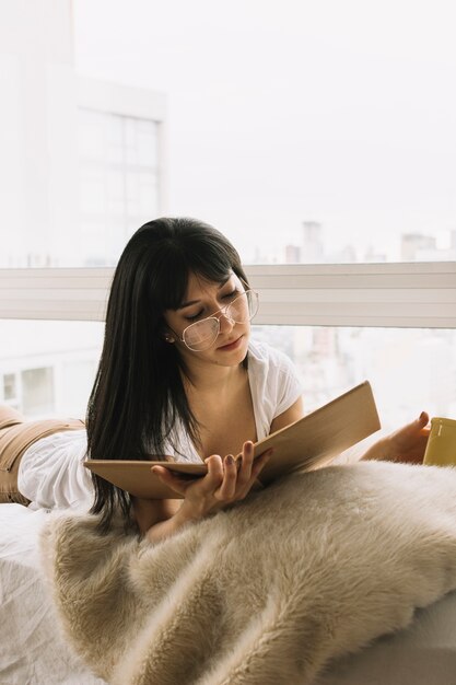 Hembra joven en vasos leyendo en la cama