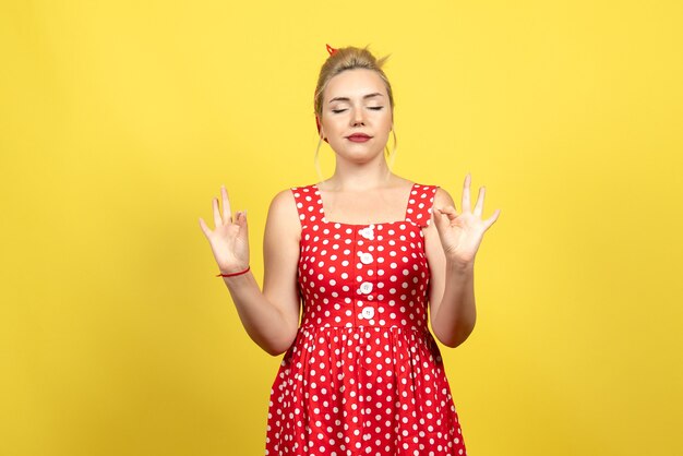 Hembra joven en vestido rojo de lunares cerrando los ojos en amarillo