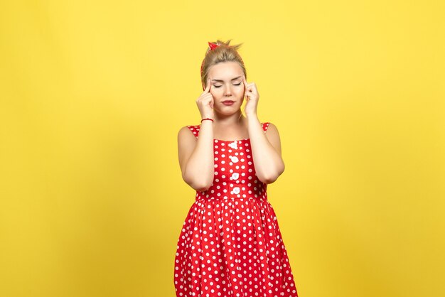 Hembra joven en vestido rojo de lunares cerrando los ojos en amarillo