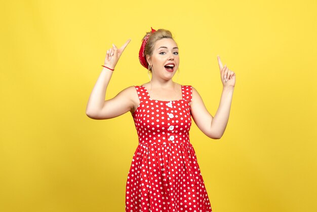 Hembra joven en vestido rojo de lunares levantando los dedos sobre amarillo