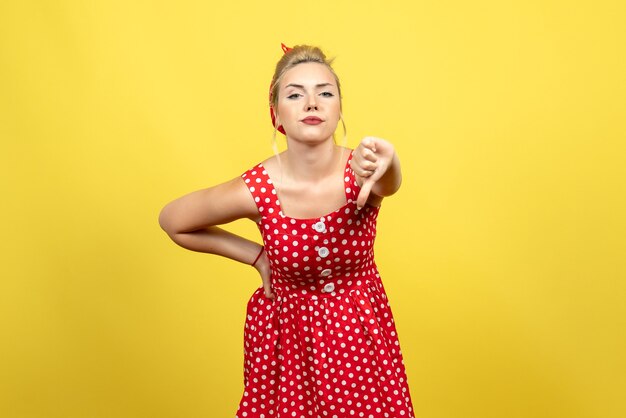 Hembra joven en vestido rojo de lunares mostrando signo diferente en amarillo