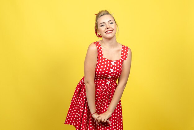 Hembra joven en vestido rojo de lunares posando felizmente en amarillo