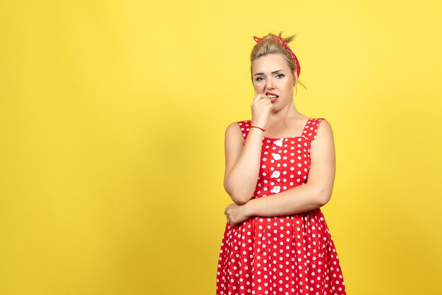 Hembra joven en vestido rojo de lunares sintiéndose nerviosa en amarillo