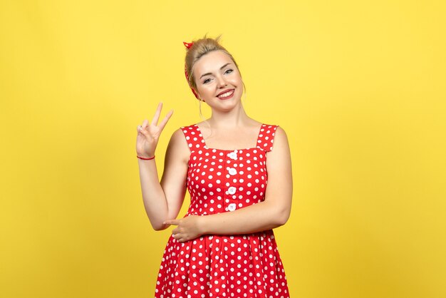 Hembra joven en vestido rojo de lunares sonriendo y posando en amarillo