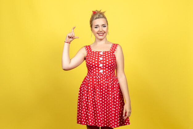 Hembra joven en vestido rojo de lunares sonriendo sobre amarillo