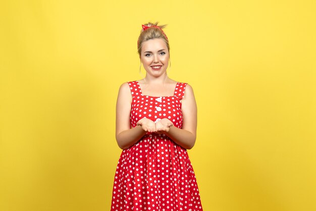 Hembra joven en vestido rojo de lunares sonriendo sobre amarillo