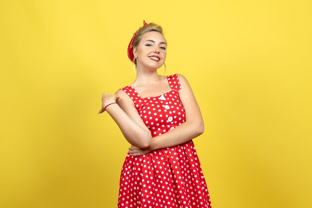 Hembra joven en vestido rojo de lunares sonriendo sobre amarillo