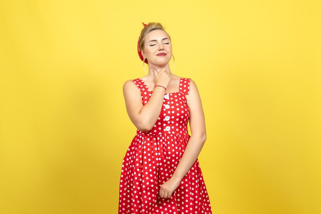 Hembra joven en vestido rojo de lunares sosteniendo su garganta en amarillo