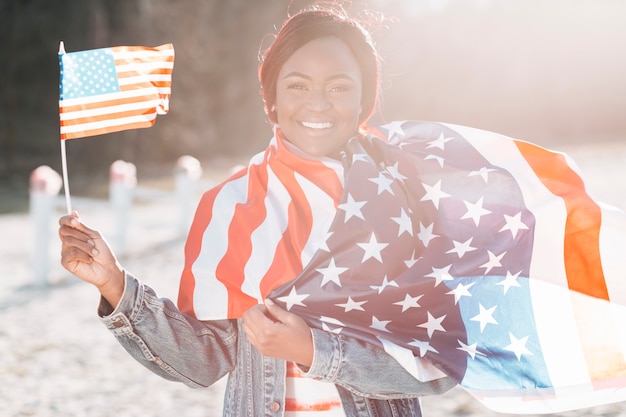 Hembra negra con banderas americanas de pie en la arena