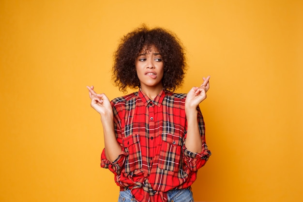 La hembra negra cruza los dedos, espera que todos los deseos se hagan realidad sobre un fondo naranja brillante. Personas, lenguaje corporal y felicidad.