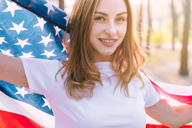 Hembra patriótica alegre con bandera americana al aire libre