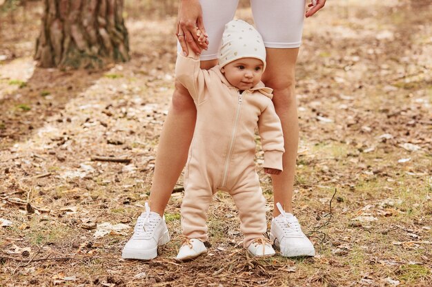 Hembra sin rostro sosteniendo la mano de la hija infantil mientras el bebé aprende a ir, familia jugando en el bosque