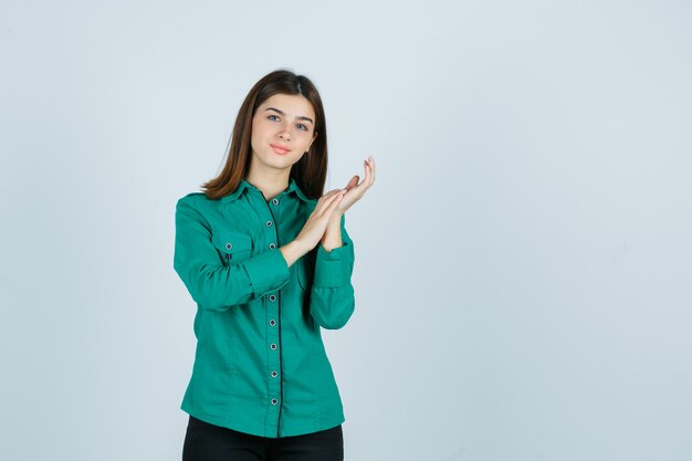 Las hembras jóvenes frotan las palmas juntas en camisa verde y lucen delicadas, vista frontal.