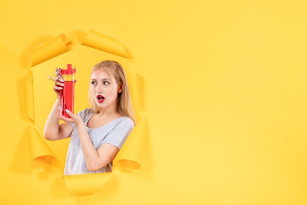 Las hembras jóvenes sosteniendo una botella roja en la pared amarilla