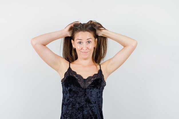 Las hembras jóvenes tomados de la mano en el pelo en camiseta negra y mirando gracioso