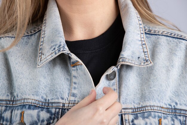 Las hembras jóvenes vistiendo una chaqueta de jean azul de pie contra una pared blanca