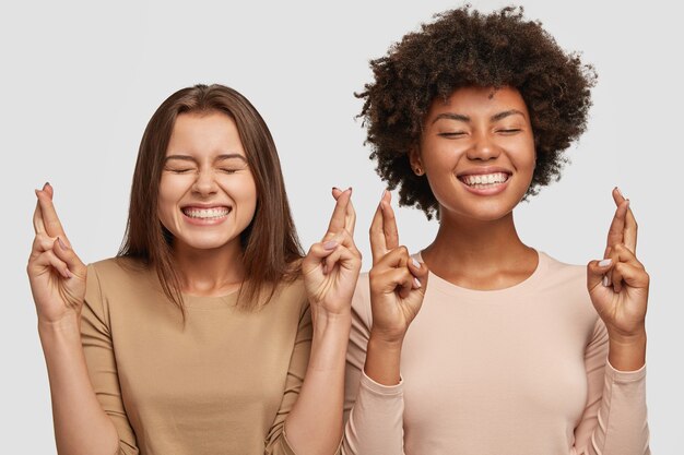 Las hembras de raza mixta satisfechas tienen sonrisas con dientes, cruzan los dedos para la buena suerte o la fortuna