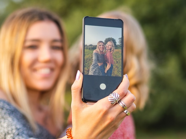 Hembras rubias felices que toman un selfie en el parque; centrarse en el teléfono