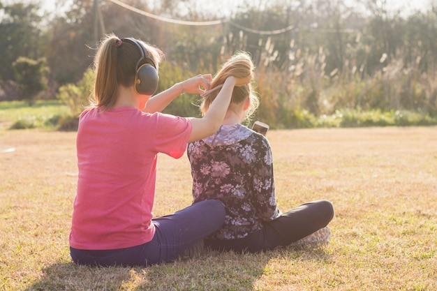 Hermana con auriculares atando el pelo de sus hermanas en el parque