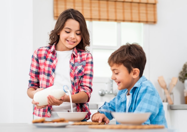 Foto gratuita hermana mayor vertiendo leche para hermanito