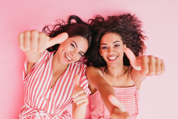 Foto gratuita hermanas de apariencia africana y cabello oscuro y rizado están descansando y mostrando que son súper con el pulgar hacia arriba.