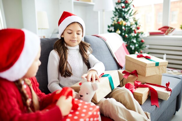 Hermanas felices sentados en el sofá y desenvolver regalos de Navidad