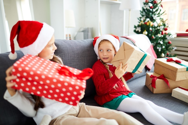 Hermanas felices sentados en el sofá y desenvolver regalos de Navidad