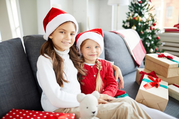 Hermanas felices sentados en el sofá con regalos de Navidad