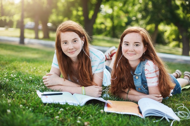 Hermanas gemelas jengibre idénticas que estudian en un parque de la ciudad. Pasar un buen rato en la universidad o en la escuela, listos para protegerse el uno al otro del acoso. Concepto de amistad y apoyo.