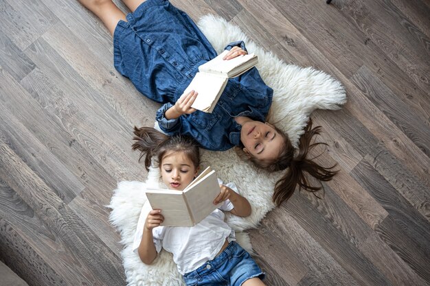 Las hermanas de las niñas leen libros tirados en el suelo, vista superior.