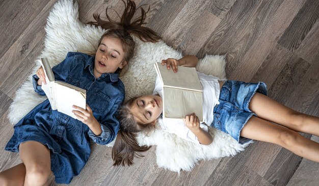 Las hermanas de las niñas leen libros tirados en el suelo, vista superior.