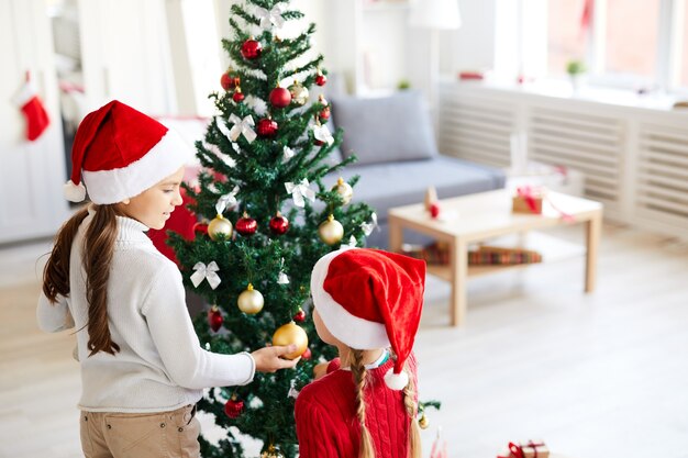 Hermanas niñas mirando el árbol de navidad, salón interior