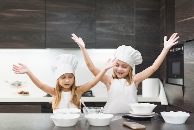Hermanas sonrientes lindas en la cocina disfrutando mientras se prepara la comida