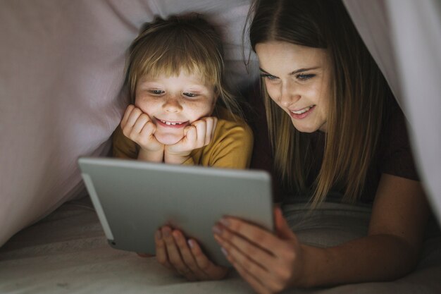 Hermanas sonrientes que miran película debajo de la manta