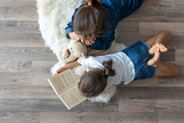 Las hermanitas están leyendo un libro con un oso de peluche tirado en el suelo en la vista superior de la habitación.