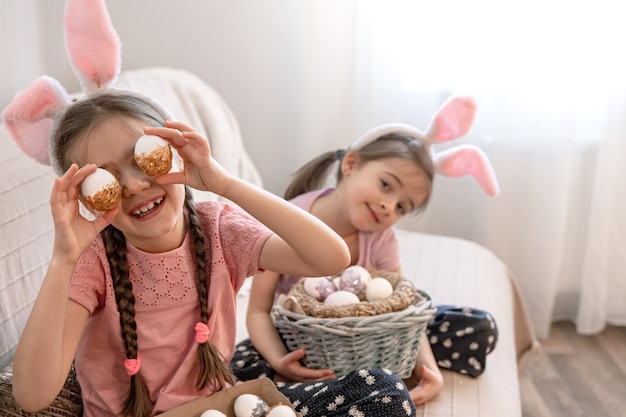 Hermanitas con orejas de conejo, con huevos de Pascua en casa en el sofá