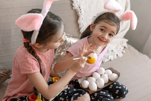 Hermanitas con orejas de conejo pintan huevos de Pascua en el sofá de casa