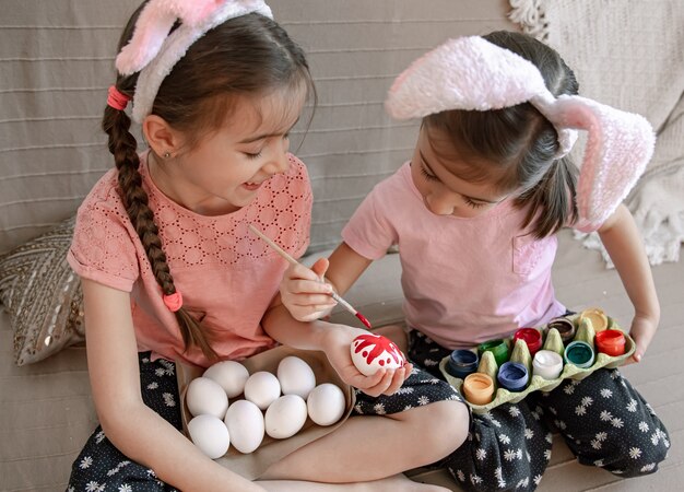 Hermanitas con orejas de conejo pintan huevos de Pascua en el sofá de casa