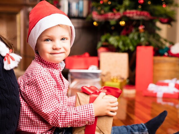 Hermano feliz con un regalo de navidad sentado en el suelo