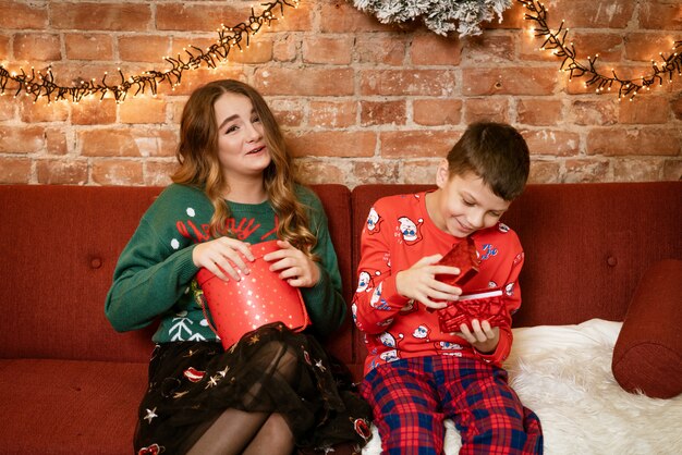 Hermano y hermana en casa en el sofá feliz abriendo regalos de año nuevo