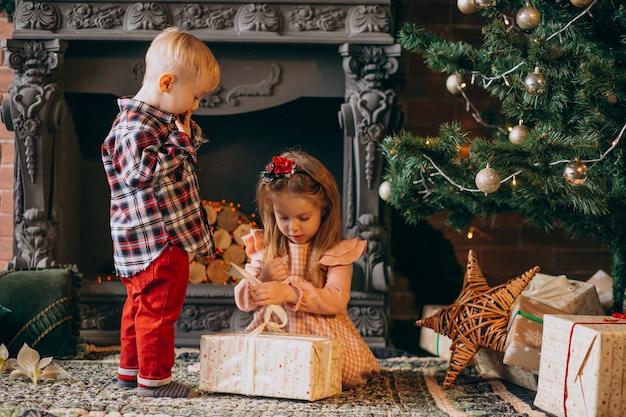 Hermano con la hermana de embalaje regalos de Navidad por el árbol de navidad