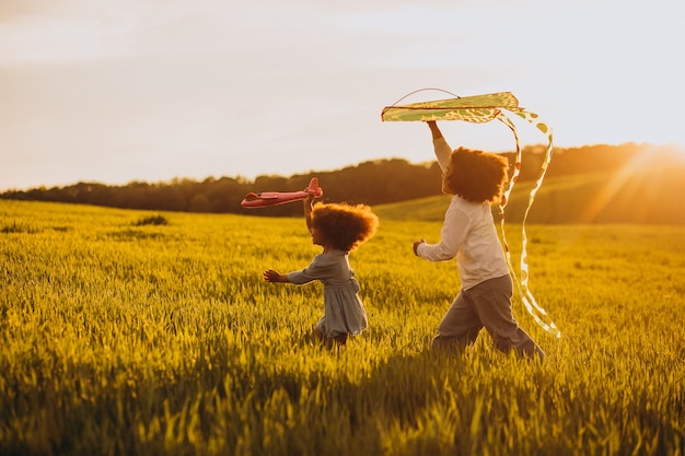 Hermano y hermana jugando con cometa y avión en el campo en la puesta de sol