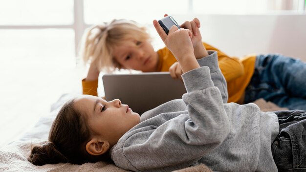 Hermanos en la cama jugando en el móvil y la tableta