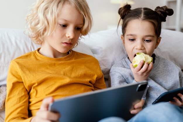 Hermanos en la cama jugando en el móvil y la tableta