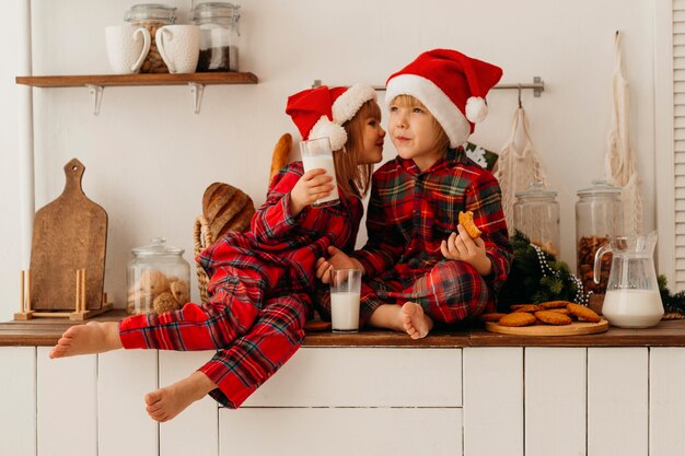 Hermanos comiendo galletas navideñas y bebiendo leche